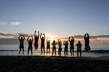 mehrere Menschen springen auf einem Steg am Meer in die Luft bei Sonnenaufgang